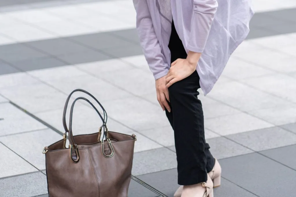 バッグを置いて左ひざを手で押さえる女性