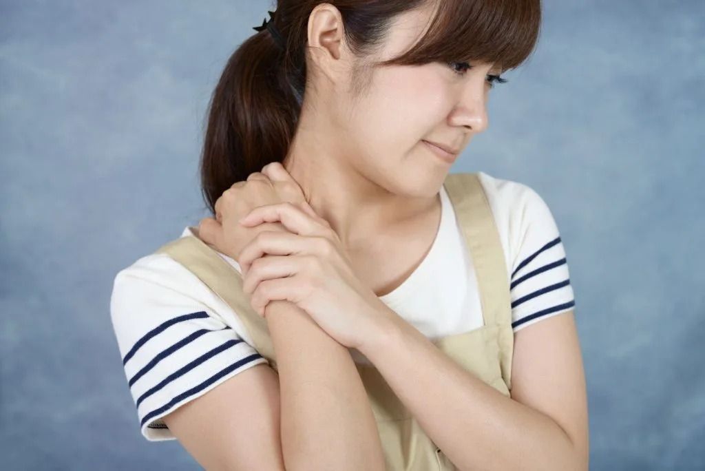 右手で首の右側を押さえる女性