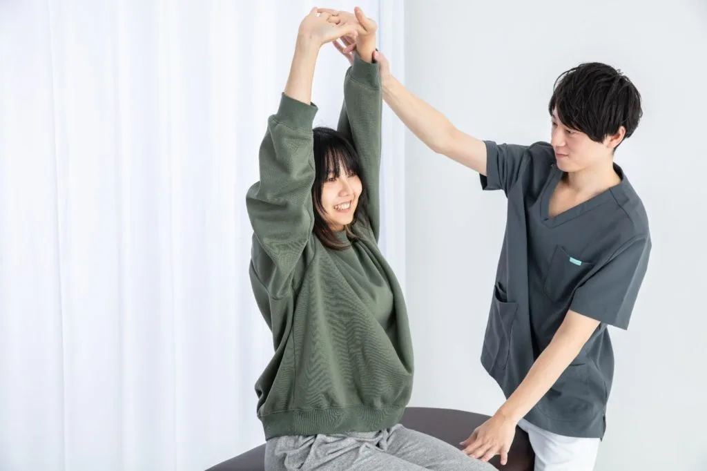 整体師に補助してもらいながら伸びをする女性