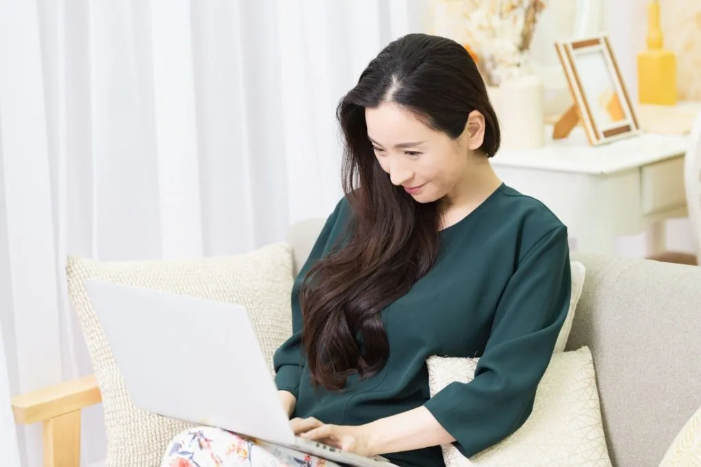 ソファーに座りながらパソコン作業をする女性
